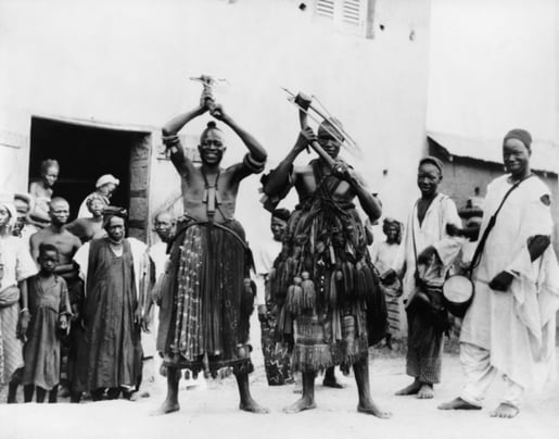 Two itinerant medicine men on a street in the village of Abeokuta, Southern Nigeria. Performing a 'hoe dance' a traditional Hausa agricultural dance. c. 1935