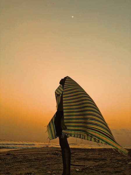 photo of an African man wearing a colorful striped blamcket over the head standing on a beach in the sunset The birth of a rainbow, Fall, Aïcha  Private Collection  © Aïcha Fall  Bridgeman Images 6037138